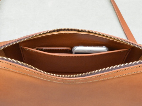 職人手作皮革單肩包內部，展示了拉鍊開合、一個手機隔層，以及光滑的棕色皮革材質，縫線清晰。