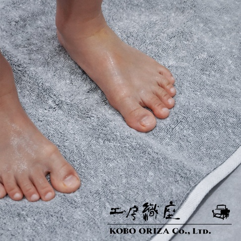 灰色的棉麻混紡雙色快乾浴墊，質地柔軟，鋪設在地面上，兩隻腳踩在上面。