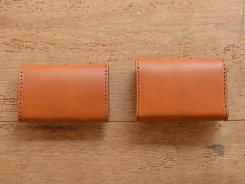兩個棕色皮革證件夾，採用手工縫線，放置在木紋背景上。