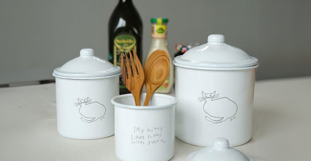 一組三個白色琺瑯儲物罐，罐身印有簡約線條貓咪圖案。其中一個罐子裝有木製叉子和湯匙，罐身寫有英文文字。