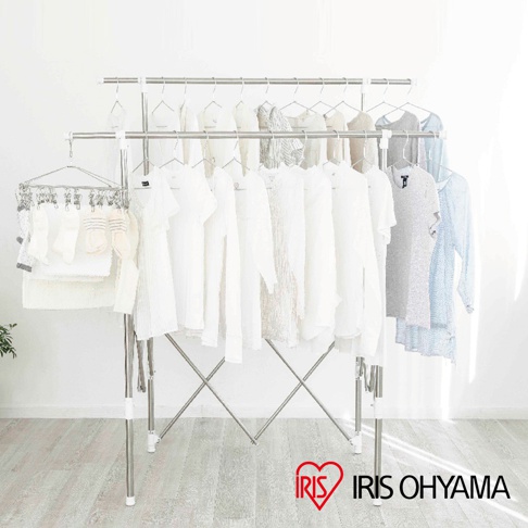 雙桿不鏽鋼曬衣架，上方掛有衣物，下方掛有襪子和毛巾。整體為銀色不鏽鋼材質，搭配白色衣物，背景為白色牆壁和淺灰色木紋地板。