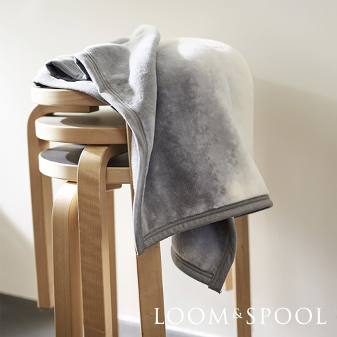 抗菌短絨舒柔單人毯，呈現漸層灰色調，質地柔軟，毯子搭在多層木製圓凳上。
