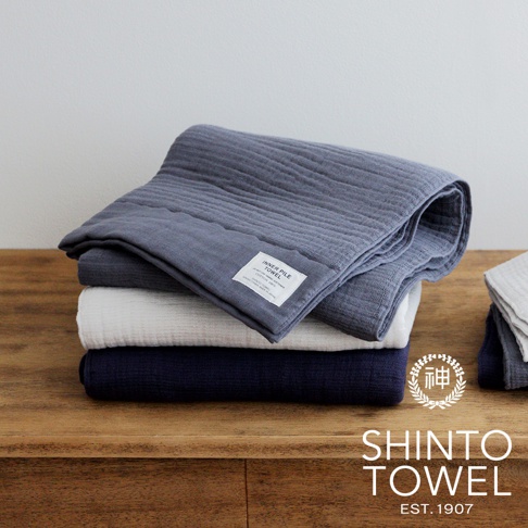 疊放的 INNER PILE 雙面紗布輕質浴巾，從上至下顏色為炭灰色、白色與海軍藍。浴巾表面有細緻的條紋紋理，其中炭灰色浴巾上縫有白色標籤。