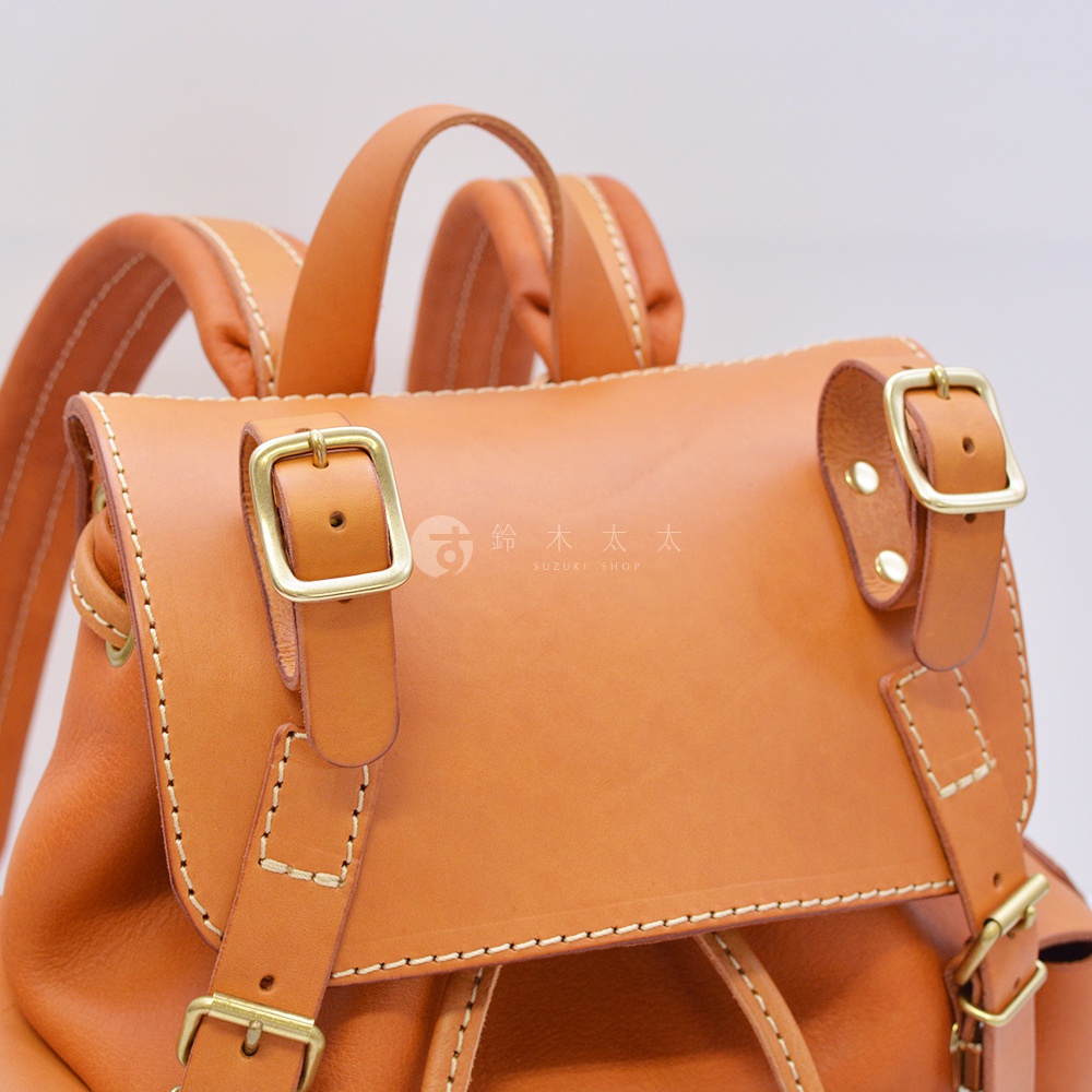 職人手作皮革復古風旅行後背包，展示卡其色皮革材質，搭配金色金屬扣環和縫線細節。