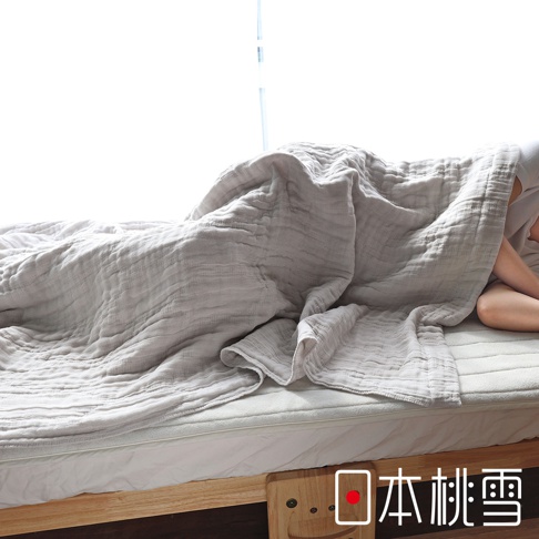 日本桃雪五層紗透氣單人被，一條灰色的薄被蓋在單人床上，被子呈現蓬鬆柔軟的褶皺感，部分露出人的腿部，床鋪下方有木製支架，右下角有日文品牌標識。