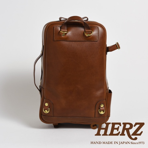 棕色皮革製成的職人手作後背包，具備雙肩帶及手提把，側面有拉鍊和口袋，底部有金屬扣環。