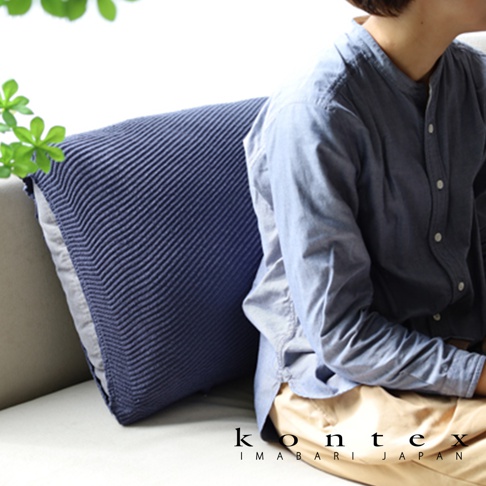 深藍色針織紋理萬用彈性枕套，搭配淺灰色枕芯，置於沙發上，旁有一名身穿淺藍色襯衫的女子。