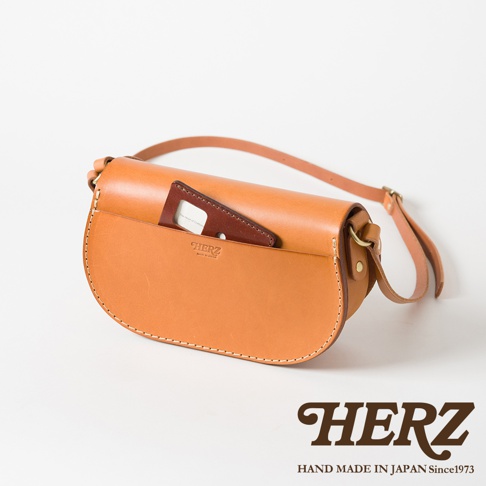 職人手作皮革迷你馬鞍包，採用天然皮革製成，呈現溫潤的棕褐色。包包為半月形設計，設有方便取放物品的前袋，內有品牌標誌。可調節長度的肩帶，適合斜挎或肩背。