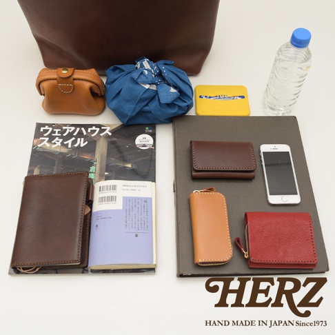 咖啡色皮革托特包內有棕色皮革零錢包、藍色布包、黃色小物盒、水瓶、一本雜誌、筆記本，以及深棕色皮夾、棕色卡夾、橘色鑰匙包和紅色小錢包。