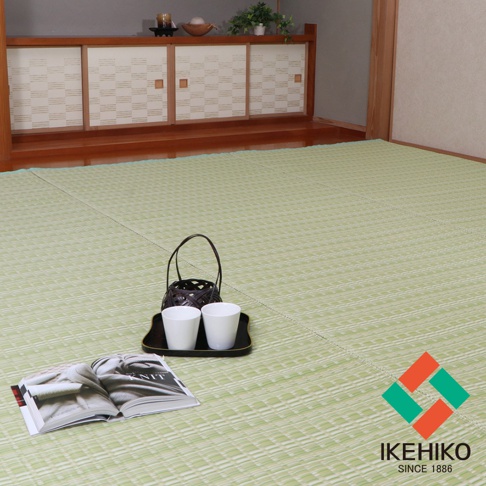 淺綠色水洗PP材質的榻榻米風格地墊，表面有細密的菱形紋理，鋪設於木質地板上。畫面前景有一本打開的雜誌，上方擺放著一個黑色托盤，托盤上有兩個白色杯子和一個竹編提籃。