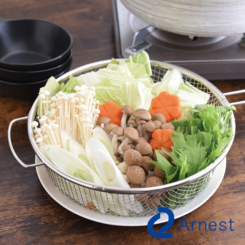 不鏽鋼手持料理濾網盛裝著多種食材，包含金針菇、鴻禧菇、蔥段、白菜、紅蘿蔔花和綠葉蔬菜，置於白色盤上，背景為木紋桌面與鍋具。