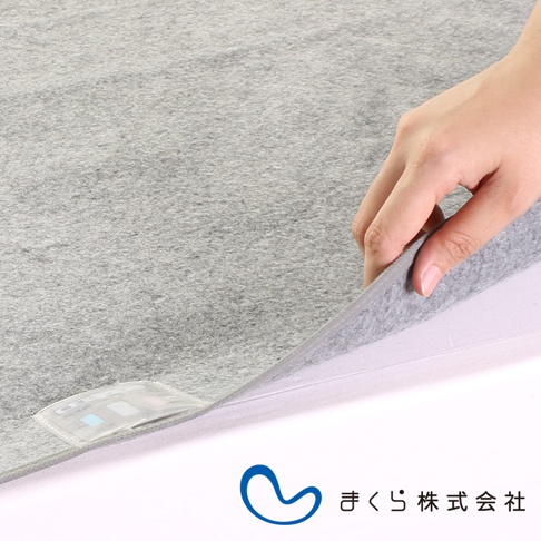 淺灰色單人備長炭防潮床墊，布料表面紋理細膩，手部掀開床墊一角，露出白色內層。床墊一角有標籤。