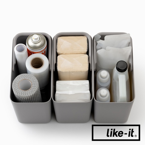 like-it 品牌標誌旁的灰色分隔收納盒，內部裝有清潔用品，包括噴霧罐、捲筒狀的保鮮膜、兩疊淡黃色物品，以及白色包裝的紙巾、兩瓶灰色蓋子的液體和一個白色瓶裝液體。