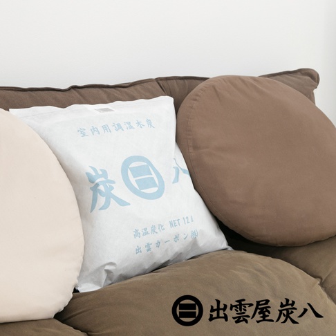 白色包裝袋裝有大型室內調濕木炭，袋上有藍色日文標示，產品置於棕色沙發上。