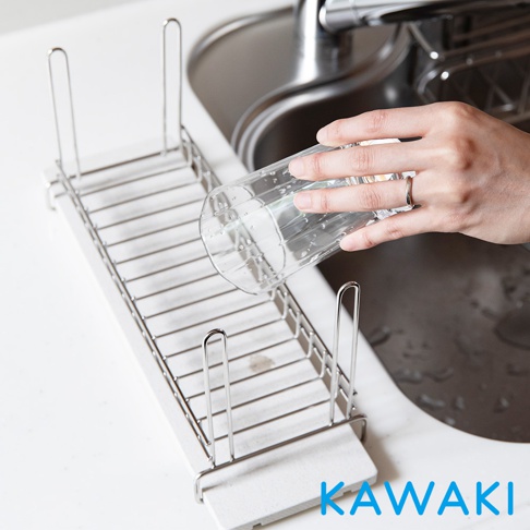 銀色金屬網架搭配白色珪藻土底座，用於瀝乾玻璃杯，上方有手持玻璃杯的特寫，背景是廚房水槽。