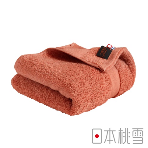 一條珊瑚橘色的今治匹馬棉毛巾，材質柔軟，毛圈細緻，帶有品牌標籤。