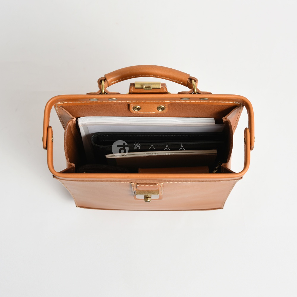 職人手作皮革杜勒斯商務後背包，淺棕色，頂部帶有提把，包內裝有筆記本和文件，採用金屬鎖扣設計。