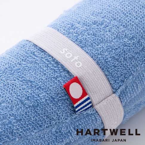 一條捲起的藍色毛巾，上面繫著白色束帶，束帶上印有 soto 字樣。毛巾材質柔軟，細節處可見今治印花。