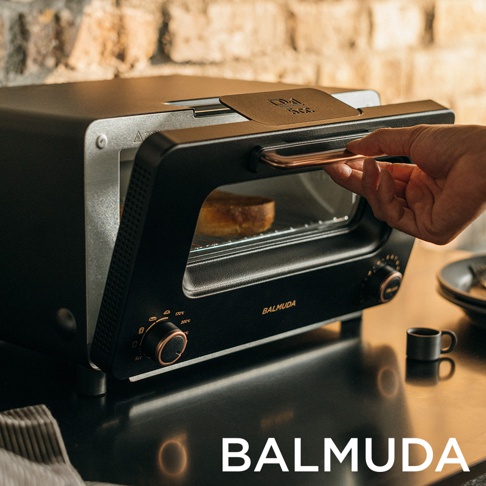 The Toaster Pro 蒸氣烤麵包機專業版 K11C-SE，黑色機身搭配玫瑰金把手，內部烤著一片吐司，上方有 BALMUDA Logo，整體呈現簡約設計。