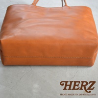 HERZ 職人手作皮革托特包，顏色為棕褐色，材質為皮革，包款為肩背款式，底部有縫線細節。