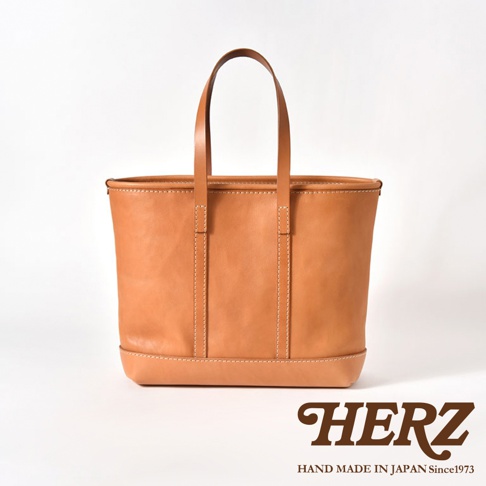 職人手作皮革經典托特包，採用天然植鞣皮革，呈現溫潤的棕褐色，簡約的方形廓形搭配手提把，車縫線清晰，展現細膩工藝。