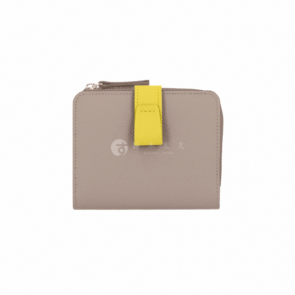 這款 Atelier nuu noble 系列雙折短夾採用灰褐色皮革製成，表面具有細緻的紋理，正面中央配有一個亮黃色的皮革搭扣設計，頂部設有 L 型金屬拉鍊，整體呈現簡約精緻的質感。