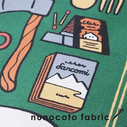 綠色帆布上印有卡通風格的圖案，包含斧頭、火柴盒、兩根火柴，以及一本標有「Sancomi」字樣和雪山圖案的書籍。