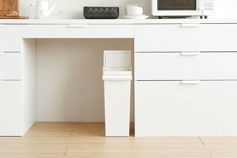 TOSTE 簡約設計風格白色按壓雙開型分類垃圾桶，置於廚房櫃下方空間，垃圾桶頂部蓋子打開，材質為塑膠。