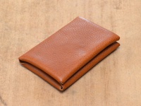 棕色皮革製成的雙開卡片收納夾，表面有細緻紋理，置於木紋背景上。