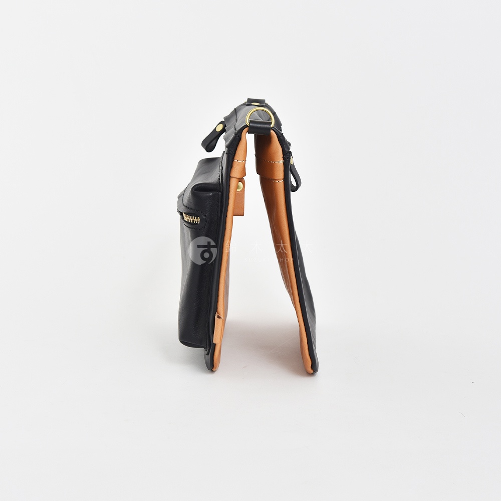 黑色皮革翻轉雙色直式斜背包，側面可見棕色內襯和金色拉鍊。