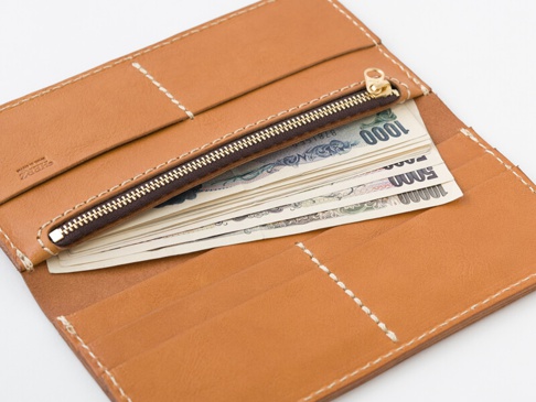 職人手作皮革簡約輕薄扁長夾，原色皮革材質，搭配白色車縫線，內部可見拉鍊零錢袋及多張日圓鈔票。