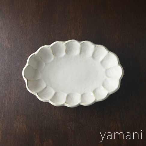 一個白色、帶有花瓣狀邊緣的橢圓形陶瓷料理盤，盤面中央平坦，邊緣有手工製作的紋理感。