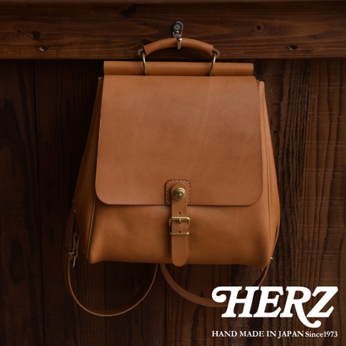 職人手作皮革後背包，呈現自然棕色，採用皮革材質，配有金屬釦環與可調節背帶，設計簡約，適合日常攜帶。
