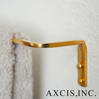 黃銅單桿毛巾架，帶有 L 型彎曲設計，固定在白色牆壁上，掛有一條灰色毛巾。