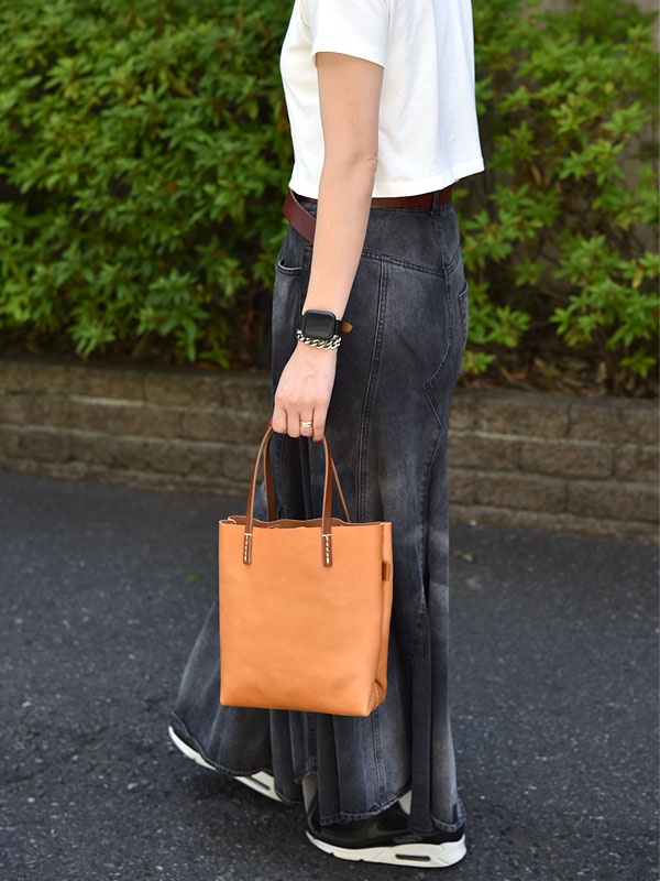 一個直立的、淺棕色皮革托特包，配有兩條短提把，包的邊緣有縫線。