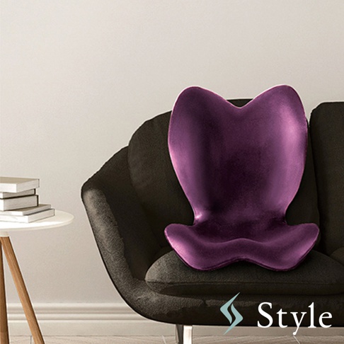 Style 品牌紫色的心形人體工學坐墊，放置於黑色沙發上，旁邊有一張白色小桌子，上面疊著幾本書。