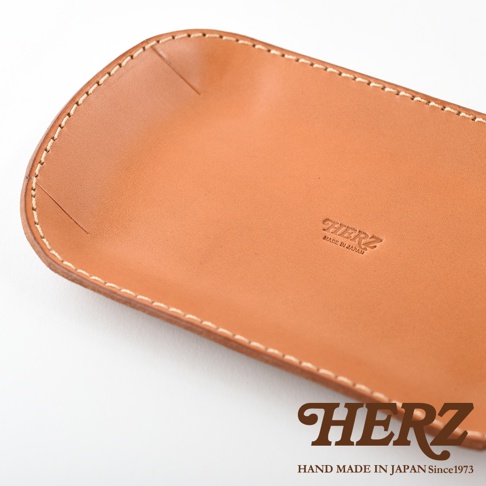 職人手作皮革小物收納盤，淺棕色，邊緣車縫線清晰，皮革表面壓印有「HERZ」及「MADE IN JAPAN」字樣。