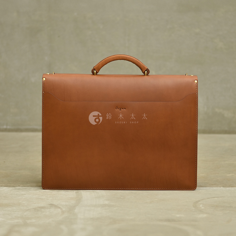 職人手作皮革Organ兩用商務公事包G-93，此款為棕褐色皮革，包身呈現簡約方形設計，配有可提式手把及金屬扣環，正面中央有燙金Logo。