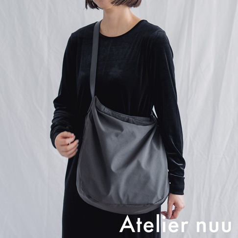 Atelier nuu ssent 肩背托特包，模特身著黑色長袖洋裝，斜挎深灰色布質包款