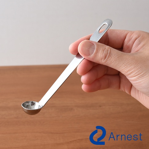 逸品物創不鏽鋼萬用醬料小勺，勺身呈長條形，帶有一個圓形掛孔，勺頭為小型圓形，整體為銀色不鏽鋼材質，由手部持握。