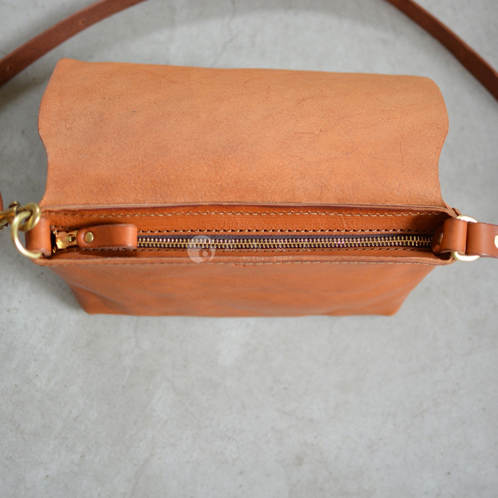 職人手作皮革斜背包，焦糖棕色，皮革紋理細緻，金色拉鍊，頂部翻蓋設計，簡約時尚。