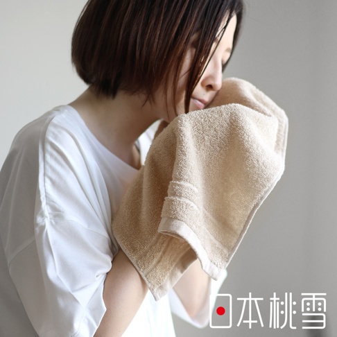 一名女子使用一條淺棕色、觸感柔軟的薄手掛耳迷你毛巾擦拭臉部，毛巾帶有兩條橫向織紋邊緣。