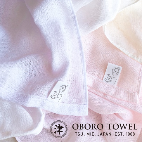 兩條三層紗專身潔膚巾，一條為白色，一條為淡粉色，質地輕柔，帶有細密的織紋，兩條潔膚巾上均有印有女性圖案的小標籤，下方有 OBORO TOWEL 商標。