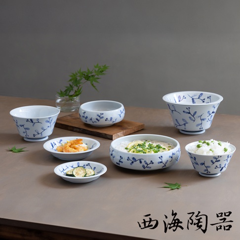 六件式白色陶瓷碗盤組，飾有藍色植物花紋，包含不同尺寸的碗，其中一些盛有食物，如麵條、米飯、炸蝦和櫛瓜片。