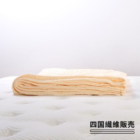 淡黃色舒芙蕾透氣涼被，無棉款，材質輕薄，表面有細緻的舒芙蕾織紋，疊放於白色床墊上。