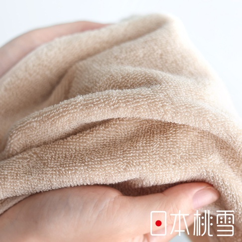 一隻手拿著一條淺棕色的毛巾，毛巾的材質細膩柔軟，上面有日文「日本桃雪」的標誌。