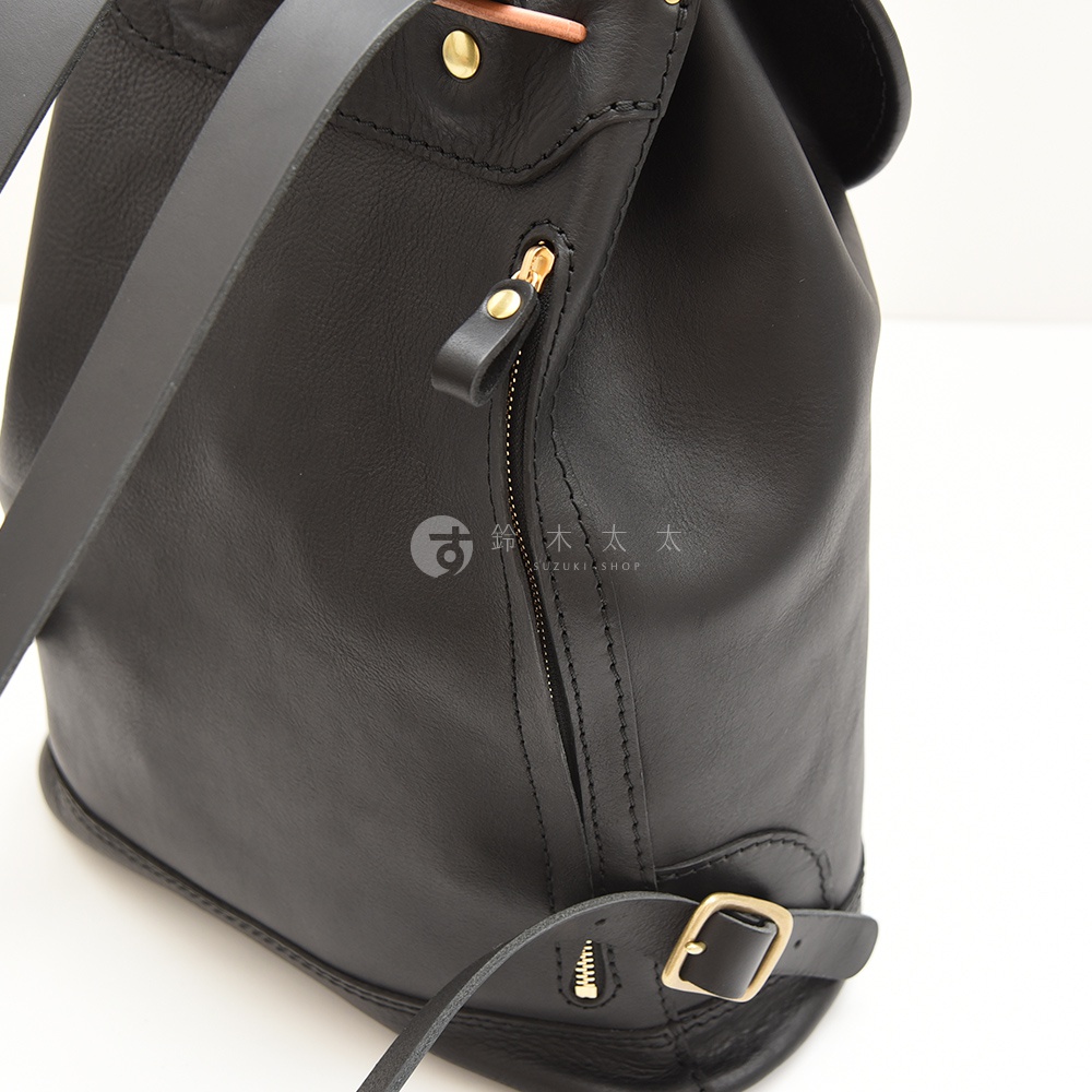 黑色皮革單扣束口後背包，設有拉鍊側袋及可調節肩帶。