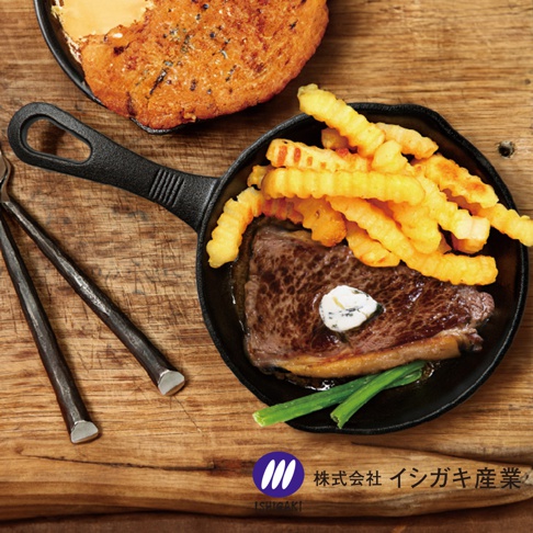 黑色鑄鐵平底鍋，內有煎牛排、炸薯條和青蔥，旁邊是烤麵包和餐具。