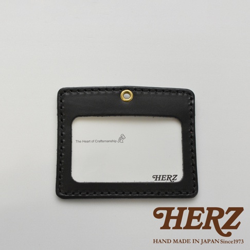 黑色皮革橫式證件識別夾，配有金屬掛孔，透明證件視窗，內部印有「The Heart of Craftsmanship」字樣與圖案，以及「HERZ」品牌標誌。