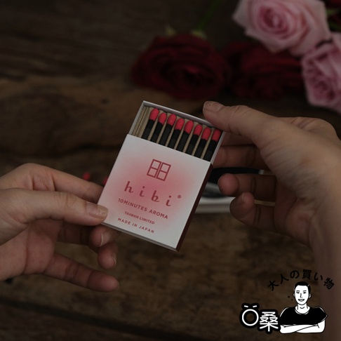 一盒裝有九支香氛火柴，火柴頭為紅色，火柴身為黑色，包裝盒為白色，印有粉色漸層與紅色品牌標誌，標示「hibi 10MINUTES AROMA TAIWAN LIMITED MADE IN JAPAN」。